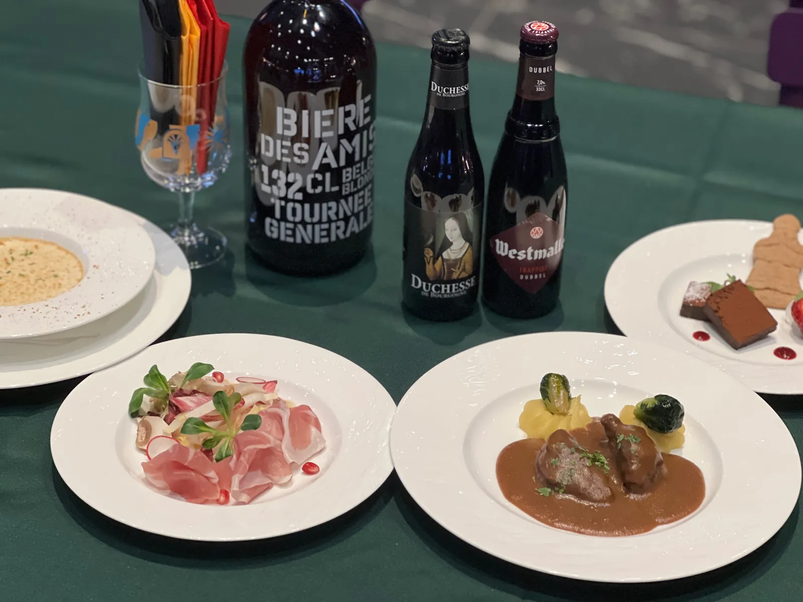 The four dinner courses plated on the green cloth, with the three Belgian beers behind them